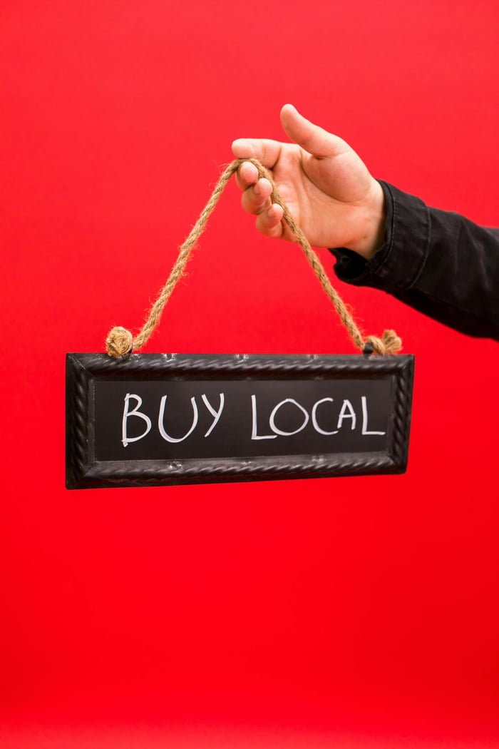 Person holding a 'Buy Local' sign suspended on ropes, promoting local business.