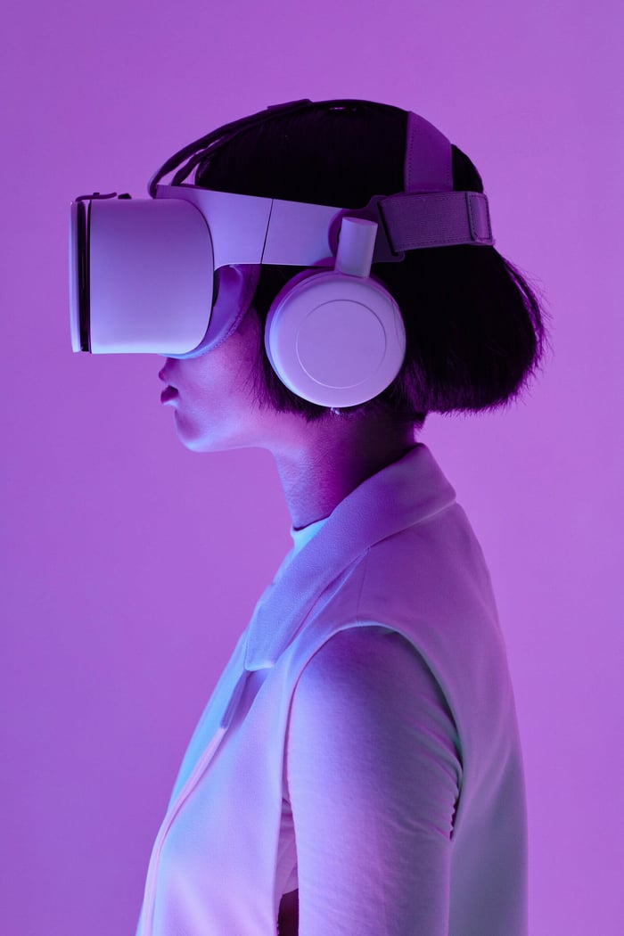 Side profile of a woman wearing VR goggles in a studio with purple lighting, embodying future tech.