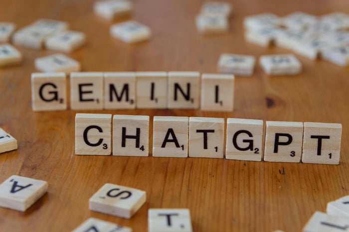 Close-up of wooden Scrabble tiles spelling Gemini and ChatGPT on a wooden surface.